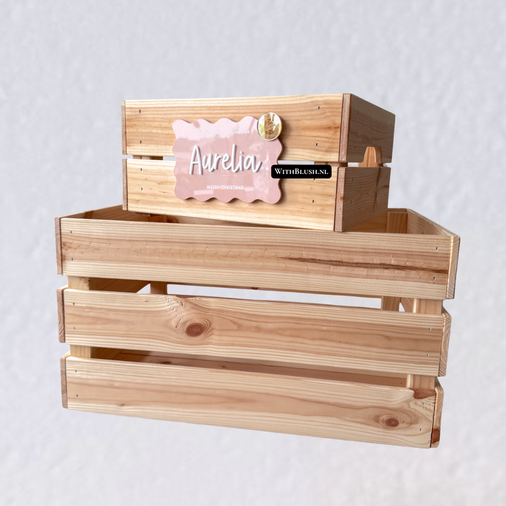Gepersonaliseerde houten kerstkist met naamlabel, kan gevuld worden met kerstitems zoals een boek en pyjama. De kist is voorzien van twee handvatten aan de zijkanten en een feestelijk label met naam, bevestigd met klittenband.