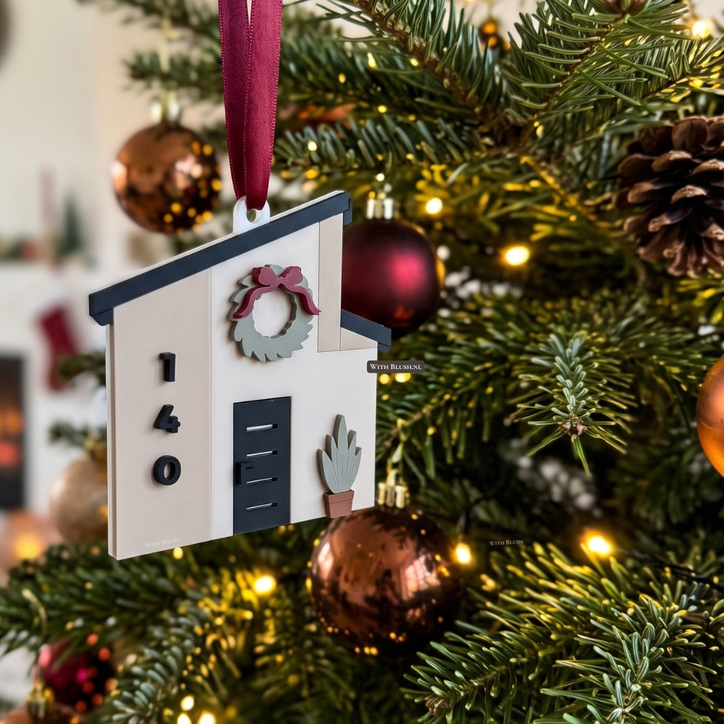 Gelaagd 3D-kerstornament van een modern miniatuurhuisje met asymmetrisch dak, huisnummer en voordeur, als kerstversiering voor een nieuwe woning.
