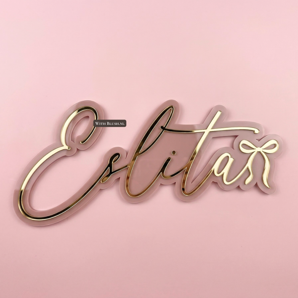 Gepersonaliseerd 3D naambord van de naam Eslita. Het dubbellaagse wandbord heeft een zachtroze achtergrond met daarop glanzende gouden letters en een elegant strikje aan het uiteinde, ideaal als decoratie voor de babykamer.