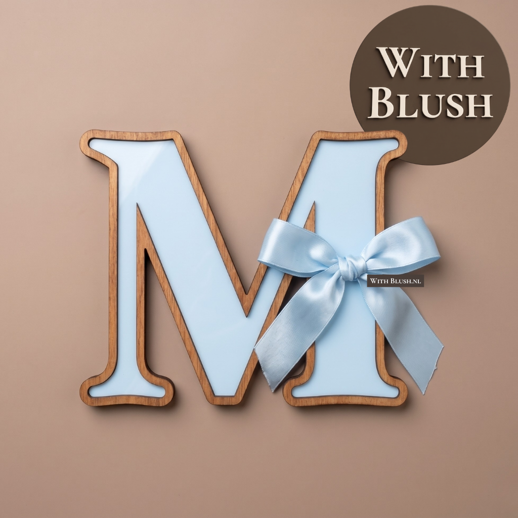 Een op maat gemaakt 3D letterbord van de letter M, ideaal als kraamcadeau of decoratie voor de babykamer. De basis is van babyblauw plexiglas, afgewerkt met een warme houten rand en een speelse, lichtblauwe satijnen lintstrik.