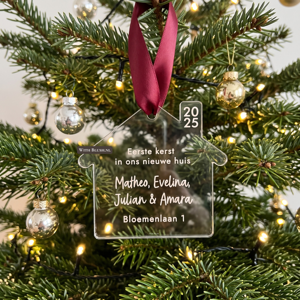 Een transparant helder plexiglas huisje kerstbal hangend in een kerstboom. Het ornament is gepersonaliseerd met namen, volledig adres en de tekst "Eerste Kerst In Ons Nieuwe Huis". Inclusief een satijnlint.