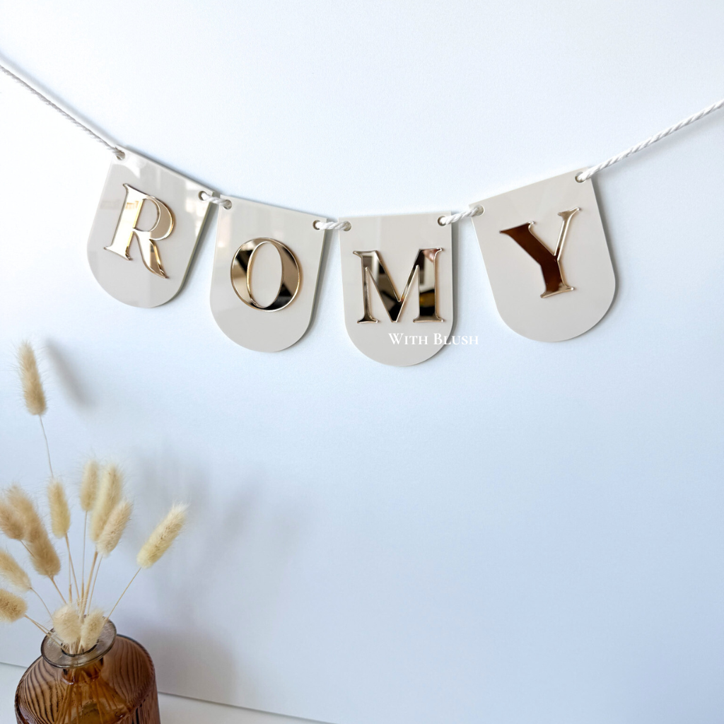 Gepersonaliseerde naamslinger met ronde vlaggetjes – Naam Romy in beige glossy plexiglas, 3D uitgesneden letters in gold mirror plexiglas.