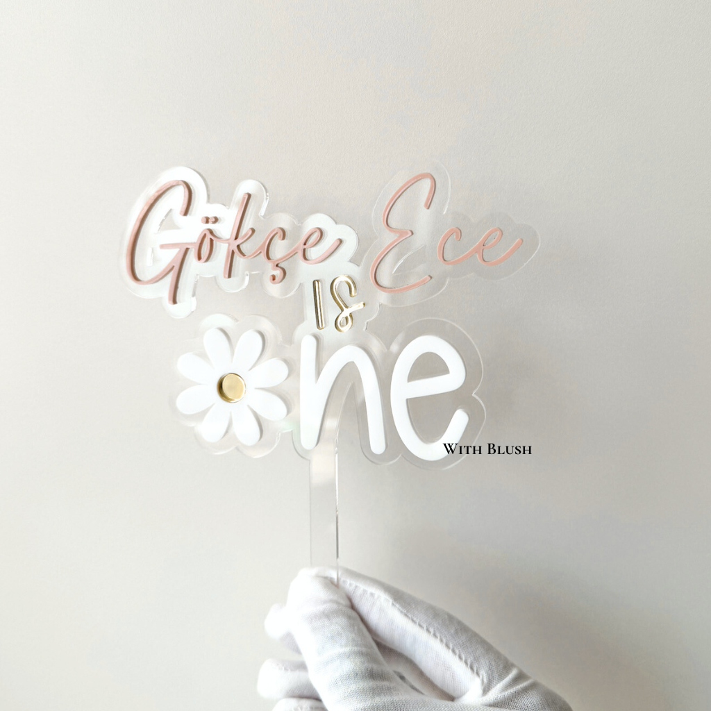 Gepersonaliseerde “Is One” taarttopper in transparant plexiglas met mauve naam in witte letters en madeliefje