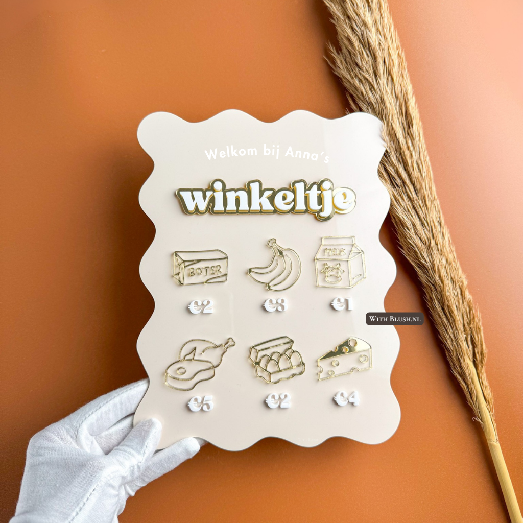 Gepersonaliseerd mini-winkeltje bordje van plexiglas met gegraveerde tekst “Welkom bij …”, WINKELTJE-letters en kleine plexiglas winkelproducten zoals boter, fruit en melk.