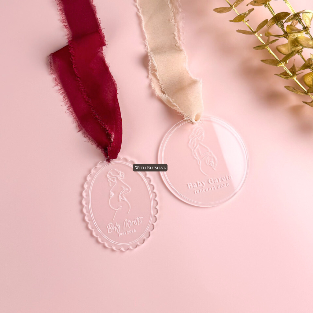 Zwangerschapsaankondiging kerstbal van plexiglas met lijntekening van mama in verwachting, gegraveerd met Baby-achternaam en verwachte datum, afgewerkt met lint.