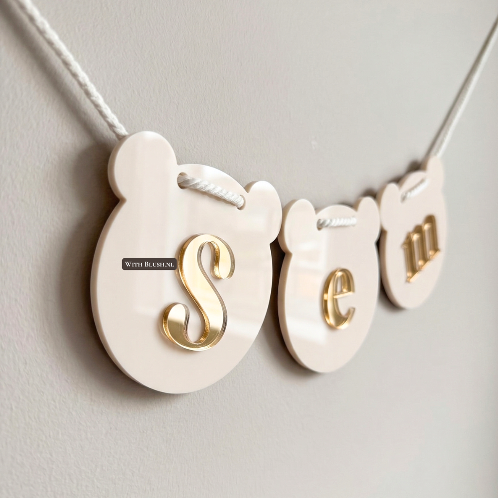 Beige plexiglas naamslinger met goudspiegel letters en vlaggetjes in de vorm van teddybeerkopjes.