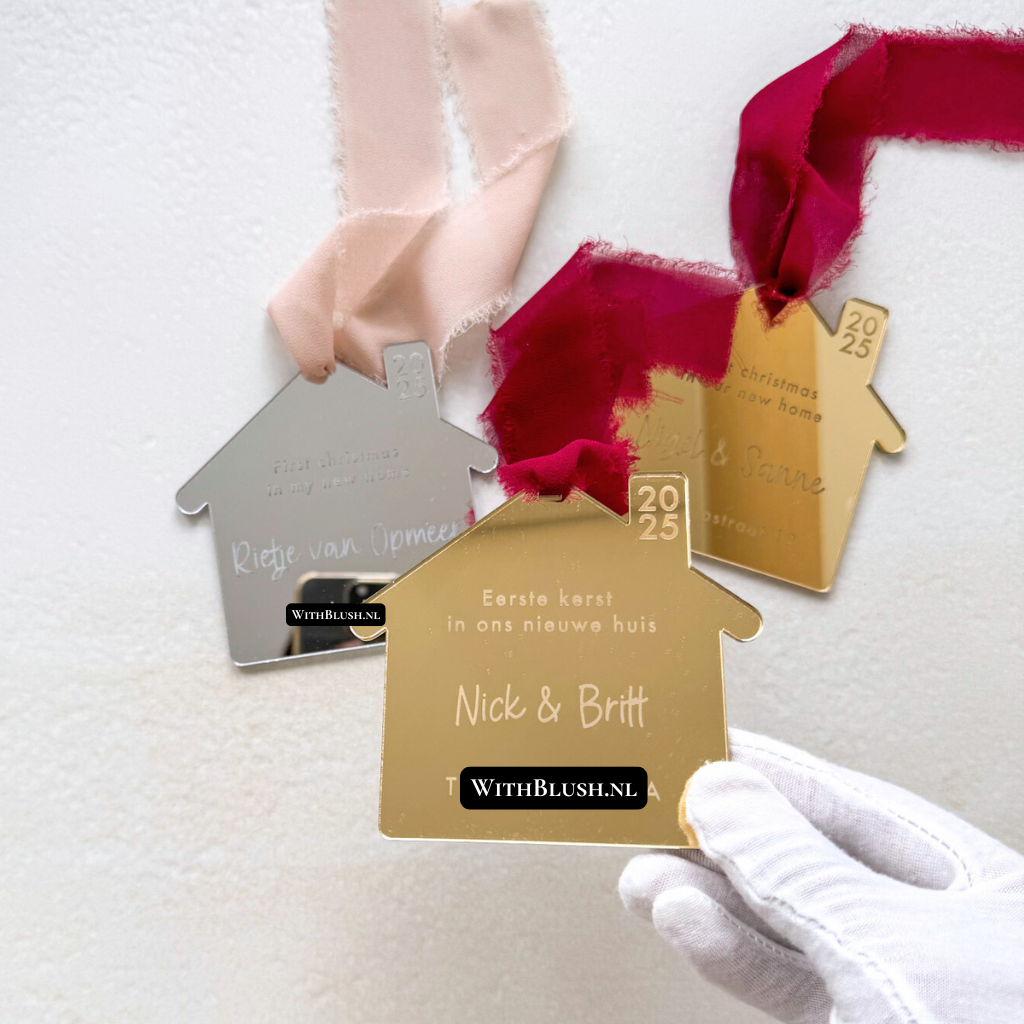 Gepersonaliseerde kerstbal in de vorm van een huisje, gemaakt van gold mirror plexiglas. De tekst “Eerste kerst in ons nieuwe huis” en namen met adres zijn gegraveerd in het midden. Luxe en warme uitstraling, compleet met lint om op te hangen — perfect als aandenken aan het eerste kerstfeest in een nieuw huis.
