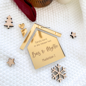 Gepersonaliseerde kerstbal in de vorm van een huisje van frosted plexiglas, met gegraveerde tekst "Eerste kerst in ons nieuwe huis", namen en adres, en een spiegelhartje uit de schoorsteen